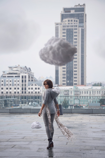 junge Frau, die auf der Straße zwischen den Wolken spaziert. Frühlingsregnerisches Wetter. abstraktes Datensparkonzept. Selektiver Fokus. - Foto, Bild
