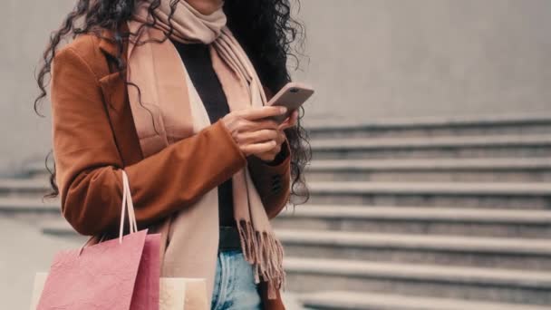 Nerozpoznatelná žena nakupující neznámá dívka v módní kabát stylové módní šála stojící ve městě držení nákupních tašek balíčky nákupy rezervace taxi auto app služby s chytrým telefonem mobilní telefon - Záběry, video
