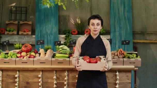 Vrouwelijke boer met een doos verse bio tomaten op de markt voor gezond voedsel, met producten van eigen bodem. Jonge gelukkige verkoper presenteert biologische natuurlijke groenten en fruit op boerenmarkt. - Video