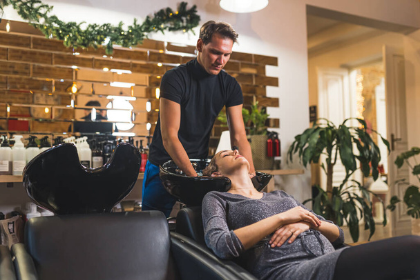 Une cliente se fait laver les cheveux au shampooing par un coiffeur masculin dans un salon de coiffure professionnel. Photo de haute qualité - Photo, image