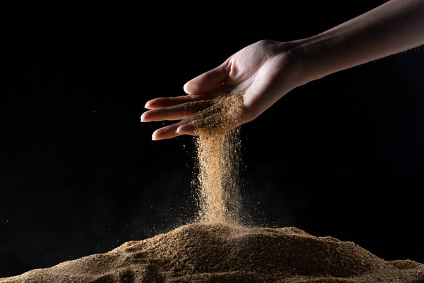 Hand releasing dropping sand. Fine Sand flowing pouring through fingers against black background. Summer beach holiday vacation and time passing concept. Isolated high speed shutter - Photo, Image