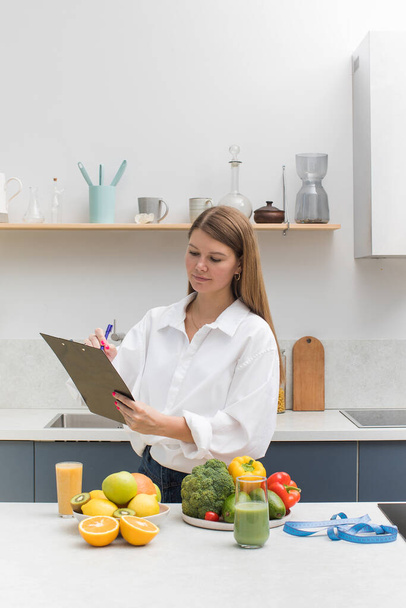 The nutritionist stands at the table with vegetables and fruits and makes a meal plan for the client. The concept of weight loss, healthy eating. - Foto, Imagen