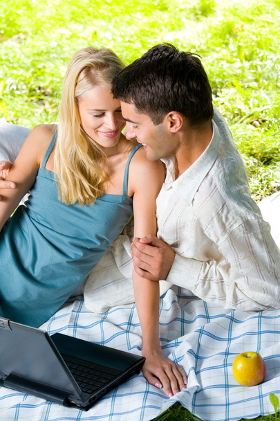 Young happy smiling couple with laptop at picnic - 写真・画像