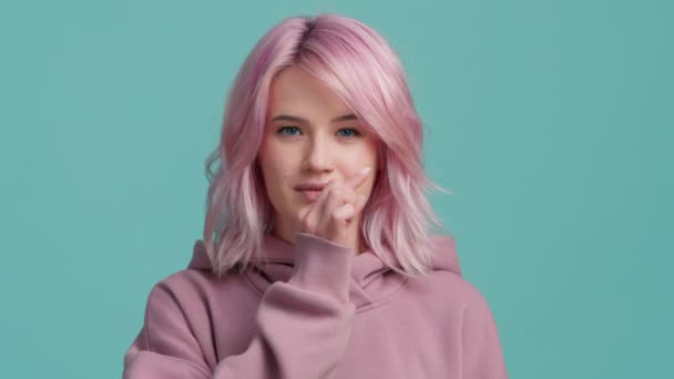 Slow motion studio shot hipster model met roze haar in pastel hoodie positief glimlachen, kijken in de camera, tonen ritsen, sluiten mond gebaar van stilte, stoppen met praten, wil niet praten 4K - Video