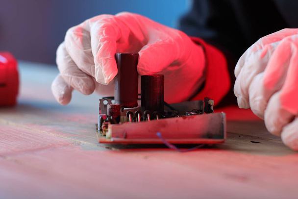 het inbrengen van een condensator in een printplaat door een persoon op een blauwe achtergrond - Foto, afbeelding
