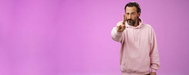 One rule listen. Serious-looking bossy focused determined adult bearded male in pink hoodie extend index finger first number scolding making statement forbid bad behaviour, purple background. - Photo, Image