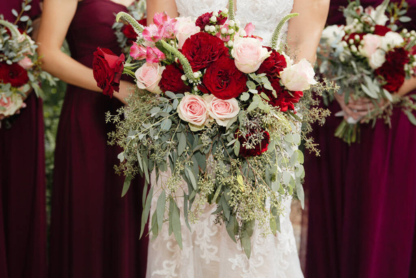 Mariée avec demoiselles d'honneur en robes magenta bordeaux avec des fleurs de mariage roses rouges et blanches profondes avec des feuilles d'eucalyptus ensemencées - Photo, image