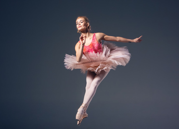Beautiful female ballet dancer on a grey background. Ballerina is wearing  pink tutu and pointe shoes. - Valokuva, kuva