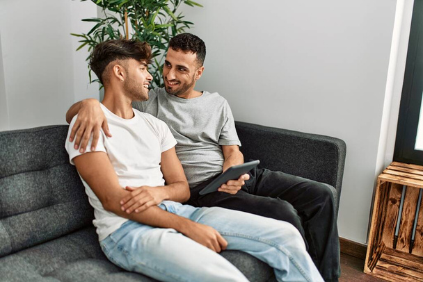 Two hispanic men couple using touchpad hugging each other at home - Photo, image