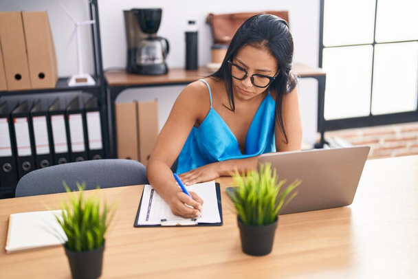 Молодая красивая латинос бизнес-работница с помощью ноутбука записи на документе в офисе - Фото, изображение