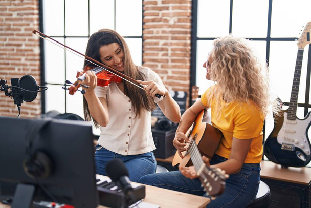 Két női zenész hegedül és klasszikus gitározik a zenei stúdióban. - Fotó, kép