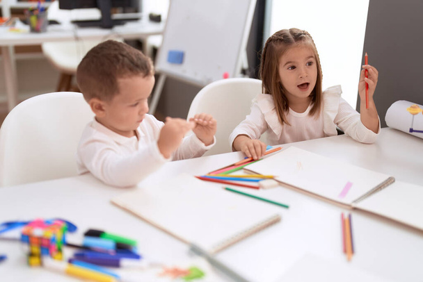 幼稚園の机の上に座ってノートを描く大人の女の子と男の子 - 写真・画像