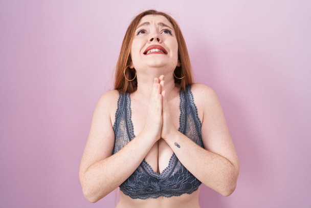 Redhead woman wearing lingerie over pink background begging and praying with hands together with hope expression on face very emotional and worried. begging.  - Valokuva, kuva