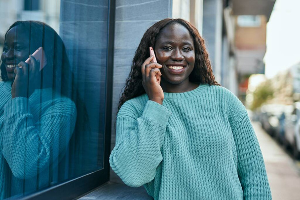 Fiatal afrikai nő mosolyog boldog beszél telefonon támaszkodva a falra - Fotó, kép