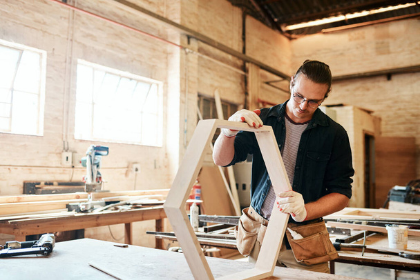 Tiene un firme control de las cosas. un joven carpintero guapo trabajando en un marco de madera dentro de un taller - Foto, Imagen
