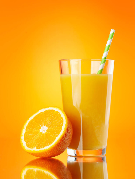 Vers sinaasappelsap in een glas en de helft van sinaasappelfruit op oranje achtergrond - Foto, afbeelding