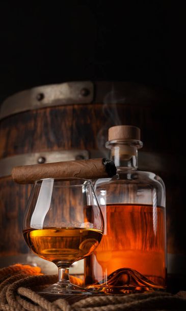 Glas und Flasche mit Cognac, Whiskey oder goldenem Rum. Vor altem Holzfass mit Kopierraum - Foto, Bild