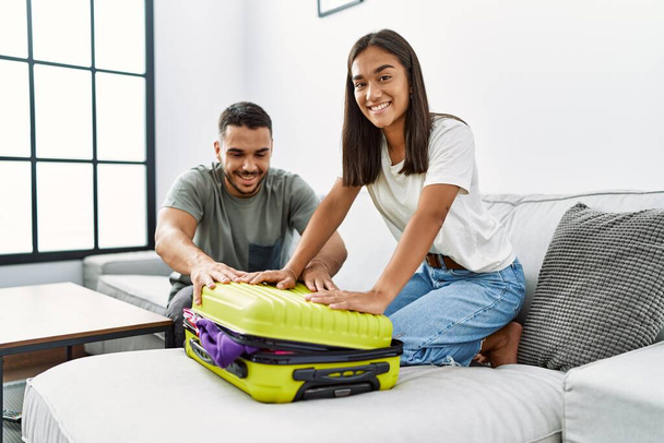 Latin man and woman couple smiling confident close travel suitcase at home - Fotó, kép