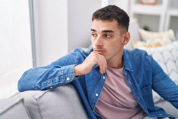 Young hispanic man sitting on sofa with serious expression at home - Photo, image