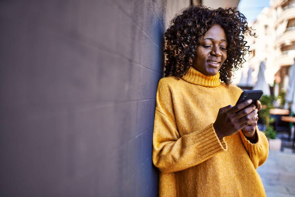 Afričanky americká žena s úsměvem sebevědomě pomocí smartphone na ulici - Fotografie, Obrázek