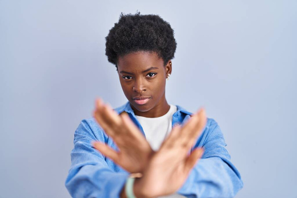 Afro-Amerikalı bir kadın mavi arka planda duruyor. Reddedilme ifadesi. Kollarını kavuşturup, avuç içlerine bakıyor.  - Fotoğraf, Görsel