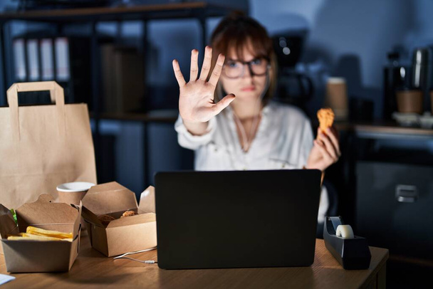 Young beautiful woman working using computer laptop and eating delivery food doing stop sing with palm of the hand. warning expression with negative and serious gesture on the face.  - Foto, Imagem