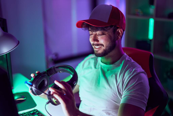 Jonge Spaanse man streamer glimlachen vol vertrouwen met behulp van de computer in gamin room - Foto, afbeelding