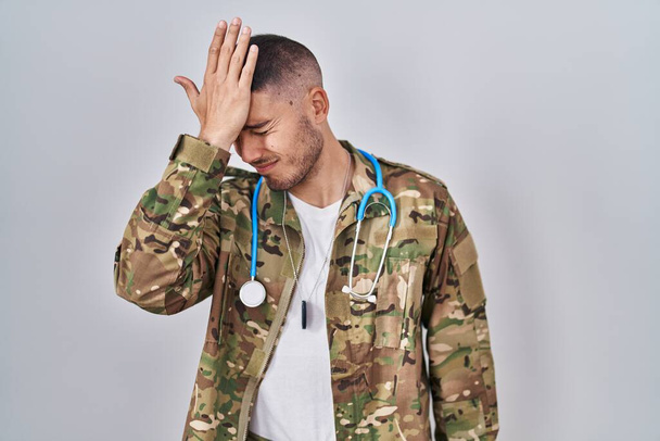 Young hispanic doctor wearing camouflage army uniform surprised with hand on head for mistake, remember error. forgot, bad memory concept.  - Foto, afbeelding