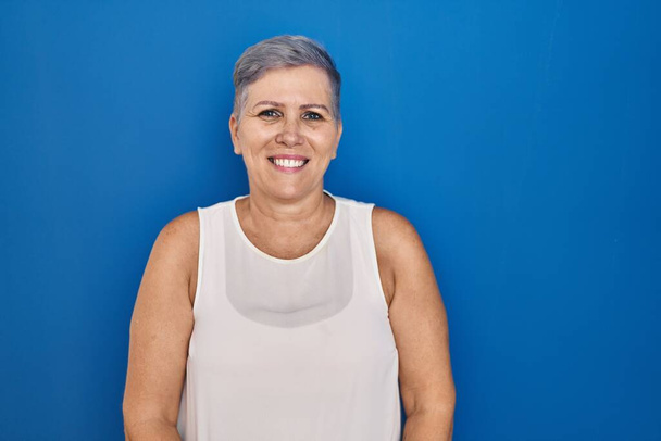 Keski-ikäinen valkoihoinen nainen seisoo sinisellä taustalla rento vakava ilme kasvoilla. yksinkertainen ja luonnollinen kameraan katsominen.  - Valokuva, kuva