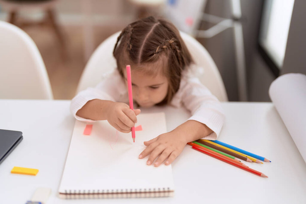 Adorable hispanic girl student sitting on table drawing on paper at classroom - Photo, Image