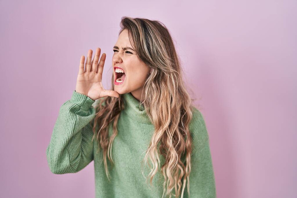 Junge kaukasische Frau vor rosa Hintergrund schreiend und laut schreiend mit der Hand auf dem Mund. Kommunikationskonzept.  - Foto, Bild