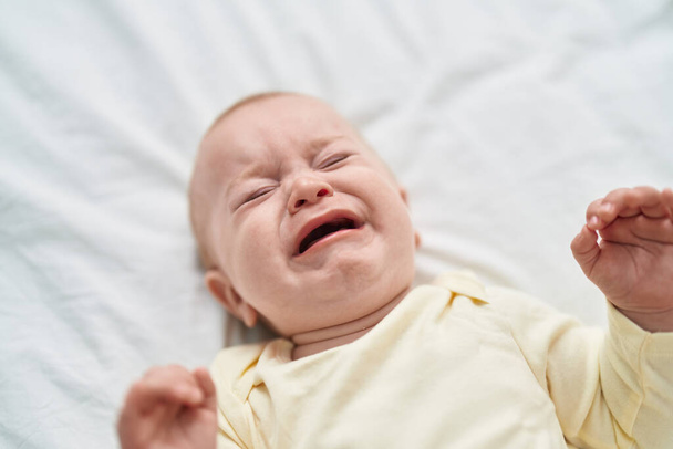 Очаровательный кавказский ребенок лежит на кровати и плачет в спальне. - Фото, изображение