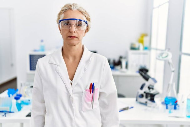 Middle age blonde woman working at scientist laboratory relaxed with serious expression on face. simple and natural looking at the camera.  - Foto, Bild