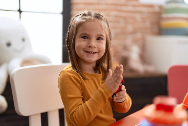 Urocza latynoska dziewczyna uśmiecha się pewnie siedząc na stole w przedszkolu - Zdjęcie, obraz