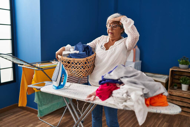 Middle age woman stressed doing chores at laundry room - Photo, Image