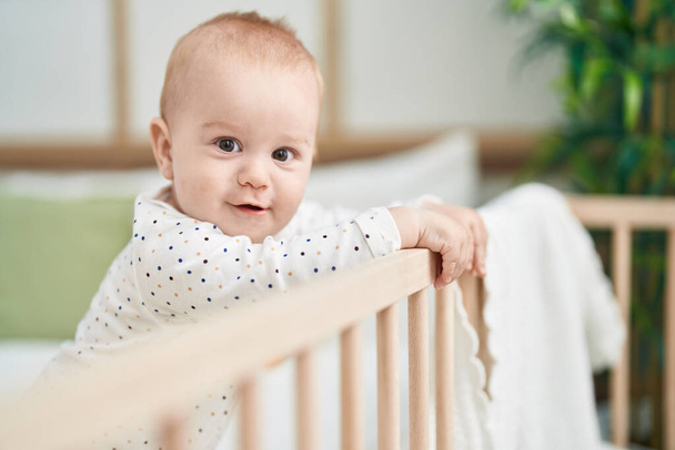 Entzückendes kaukasisches Baby lächelt selbstbewusst auf Wiege im Schlafzimmer - Foto, Bild