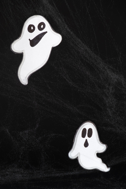 Zwei fröhliche Geister mit Gesichtern fliegen und lächeln auf schwarzem Hintergrund mit Netz. Halloween-Postkarte, ein Ort für Text - Foto, Bild