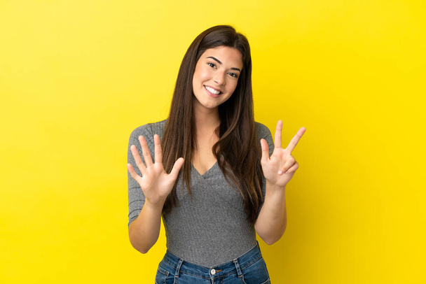 Junge Brasilianerin auf gelbem Hintergrund isoliert und zählt mit den Fingern acht - Foto, Bild