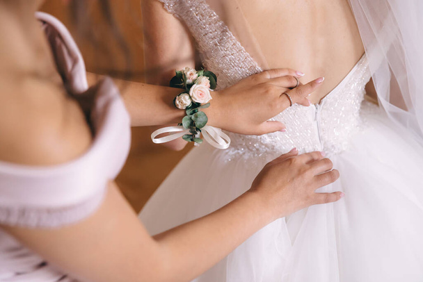 bruidsmeisje helpen bruid knopen vast op korset en het krijgen van haar jurk, voorbereiding bruid in de ochtend voor de trouwdag. - Foto, afbeelding