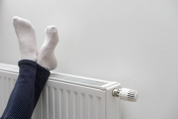 Woman warming up with feet on heater Winter socks drying on a heater. - Photo, Image