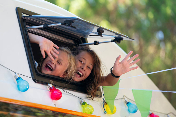 Onnelliset lapset työntävät päänsä ulos pakettiauton ikkunasta upeana retkeilypäivänä. Vanlife-käsite. - Valokuva, kuva