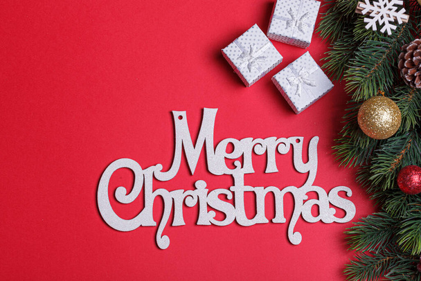 schöne Zweige eines Weihnachtsbaums mit Zapfen und Spielzeug auf rotem Hintergrund mit der Aufschrift Frohe Weihnachten in Nahaufnahme - Foto, Bild