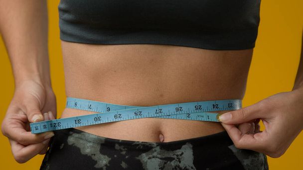 Close up female abdominal body part tummy cropped view unrecognizable sport woman with measuring tape measure waist unknown sporty slim lady girl fitness weight loss calories checking torso progress - Photo, Image