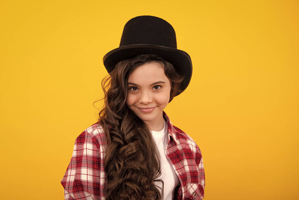 魔術師の帽子の子供の10代の女の子、黄色の背景に隔離されたシリンダー帽子。ヘッドウェアだ。服のアクセサリー。ヴィンテージスタイルで紳士のためのファッションヘッドウェア、古い古典的なシリンダー - 写真・画像
