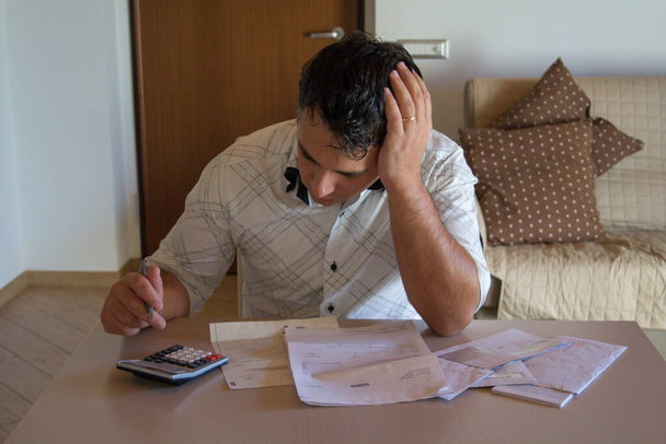 Imagem de um homem preocupado usando uma calculadora para calcular as contas que acabaram de chegar. Aumento do custo de vida devido à crise. - Foto, Imagem