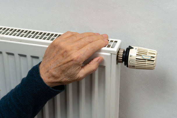 La mano de una persona mayor se calienta en un radiador de calefacción doméstica. De cerca.. - Foto, imagen