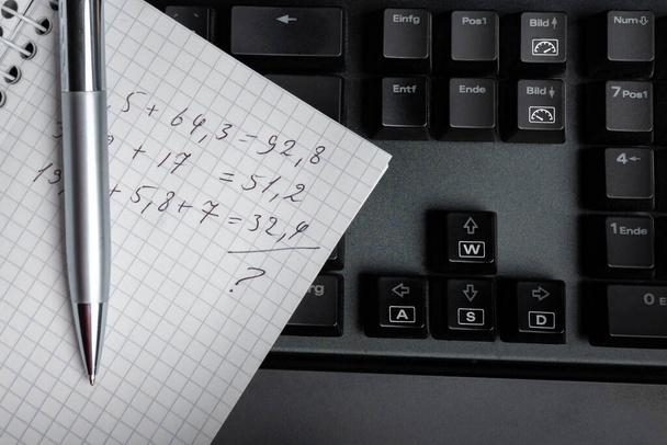 Шариковая ручка и лист заметок с арифметическими расчетами на клавиатуре компьютера. Закрыть. - Фото, изображение