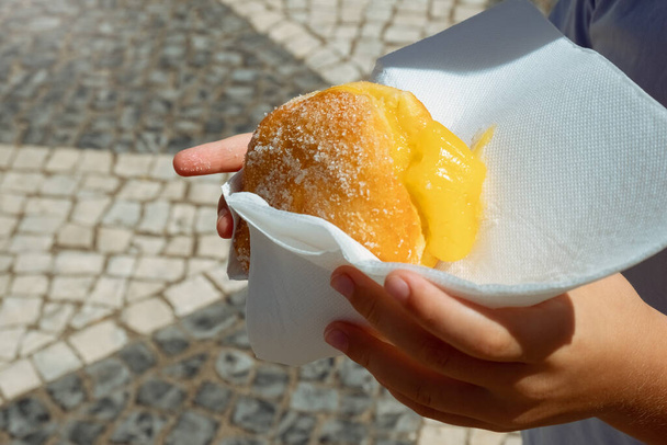 Hand holding Bola de Berlim of Berlim Ball, een Portugees gebak gemaakt van een gebakken donut gevuld met zoete eggy crème en gerold in knapperige suiker - Foto, afbeelding