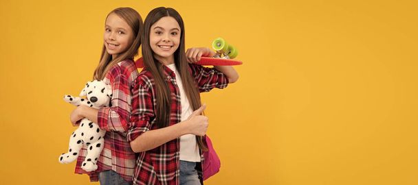 School girls friends. happy teen girls in casual checkered shirt carry backpack toy and penny board, skateboard. Portrait of schoolgirl student, studio banner header. School child face, copyspace - Photo, Image