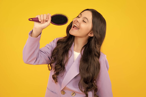 Excited teenager girl singing with comb. Child girl with brush combing hair. Girl taking haircare and hairstyle - Фото, изображение